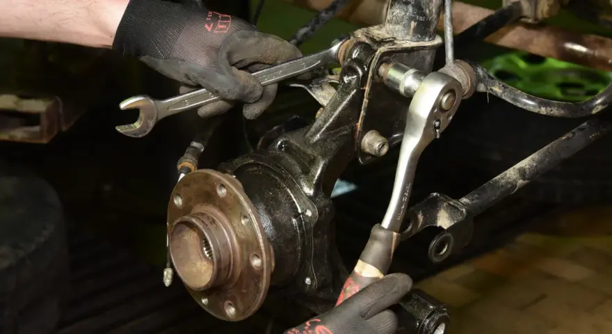 Mechanik dokręca śruby przy piaście, wymieniając łożysko w samochodzie.
