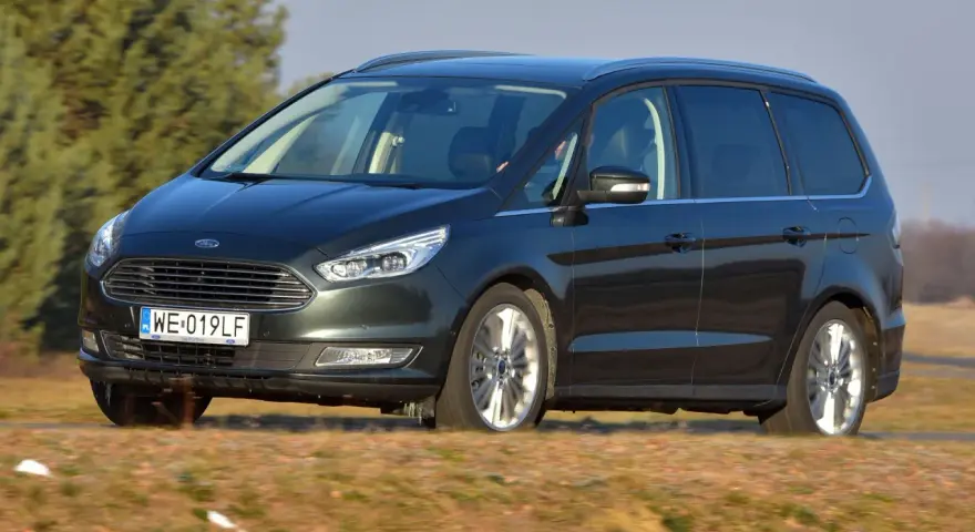 Ciemnozielony Ford Galaxy MK3 w ruchu, z polską tablicą rejestracyjną WE 019LF, przemierza wiejskie drogi.