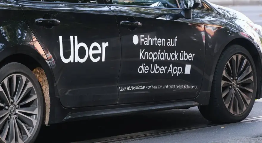 Schwarzes Auto mit "Uber" Logo. Hier erfährst du, wie kann man über Fahrer werden und Fahrten über die App buchen.