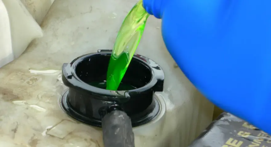 Green antifreeze is poured from a blue jug into a car's coolant reservoir. This raises the question: does antifreeze expire?