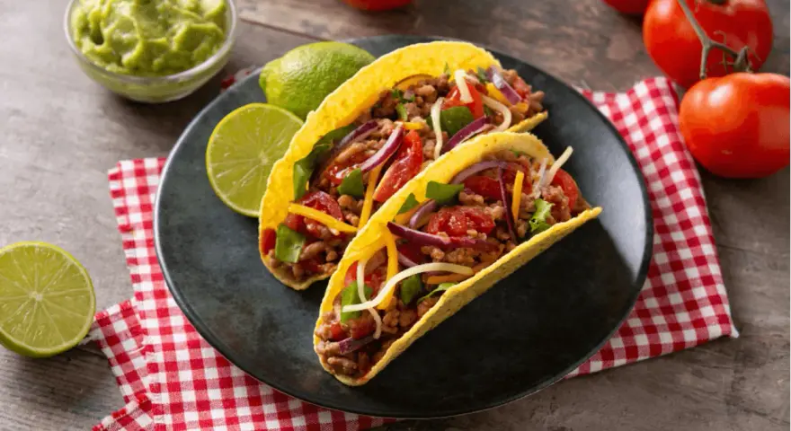 Dwa pyszne tacos z wołowiną, pomidorami, cebulą i serem, podane z limonką i guacamole.