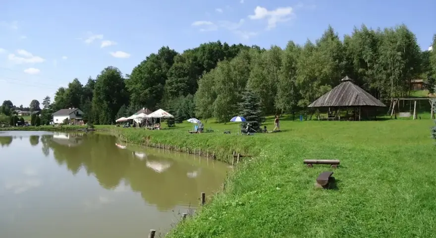 Malownicze dzikie łowiska Małopolska: spokojna woda, zielone wzgórza, drewniana altana i miejsca do wypoczynku.