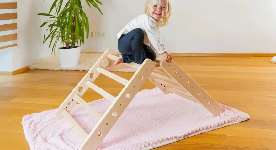 Ein fröhliches Kleinkind erkundet ein Pikler Dreieck. Ab wann Kinder damit spielen können, hängt von ihrer Entwicklung ab.