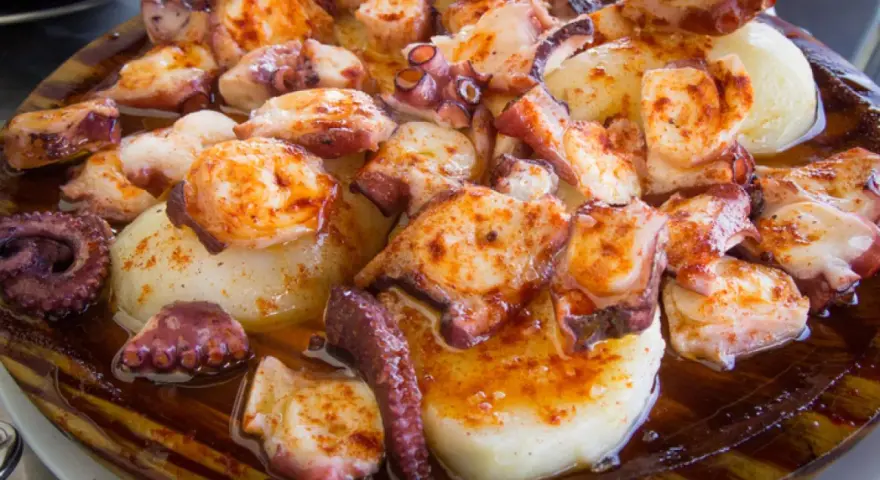 Pulpo a la gallega servido en plato de madera, con patatas cocidas y espolvoreado con pimentón.