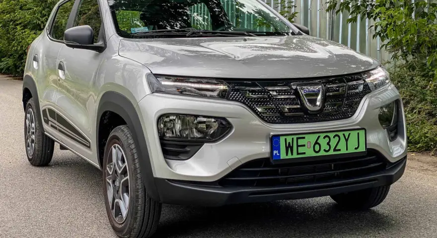 Srebrny Dacia Spring Electric z zieloną tablicą rejestracyjną WE 632YJ zaparkowany na drodze.