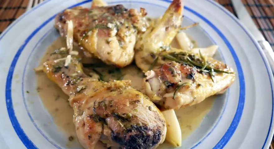 Delicioso pollo al ajillo servido en un plato azul y blanco, con trozos de pollo jugosos y dorados bañados en una salsa aromática con hierbas y ajo.