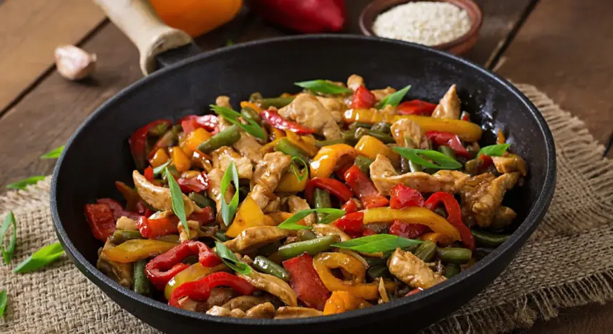 Straccetti di pollo con peperoni colorati e fagiolini, un piatto saporito e invitante servito in padella.