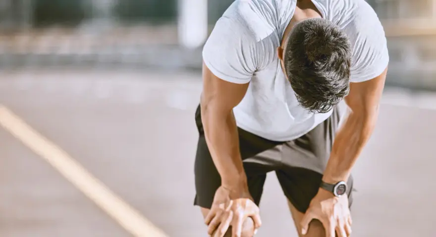 Atleta esausto con la testa china, mani sulle ginocchia, forse uno dei sintomi di overtraining.