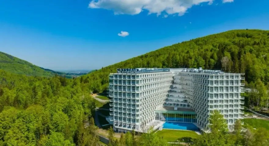 Nowoczesny Crystal Mountain Hotel Wisła otoczony zielonymi wzgórzami, z basenem i tarasami.