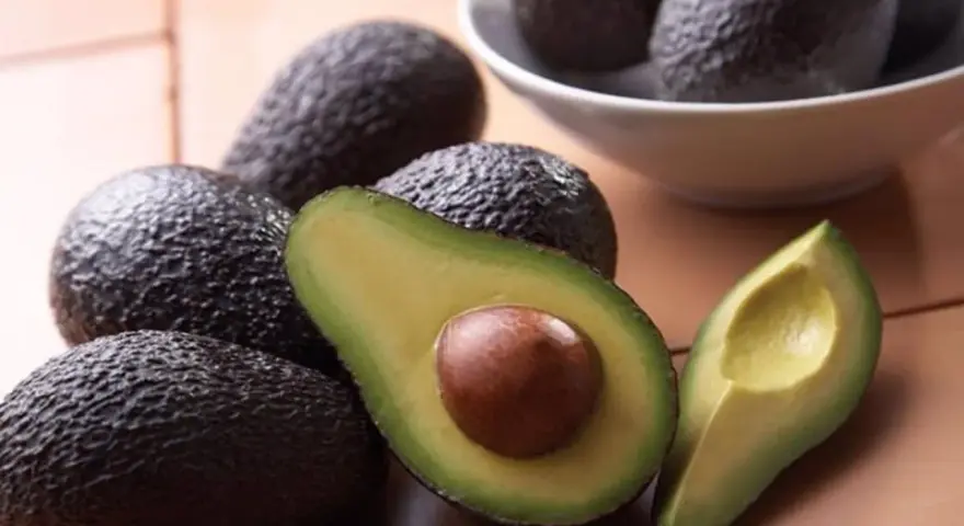 Aguacates frescos, uno cortado por la mitad mostrando su semilla, perfectos para comer aguacate todos los días y disfrutar de su cremosidad.