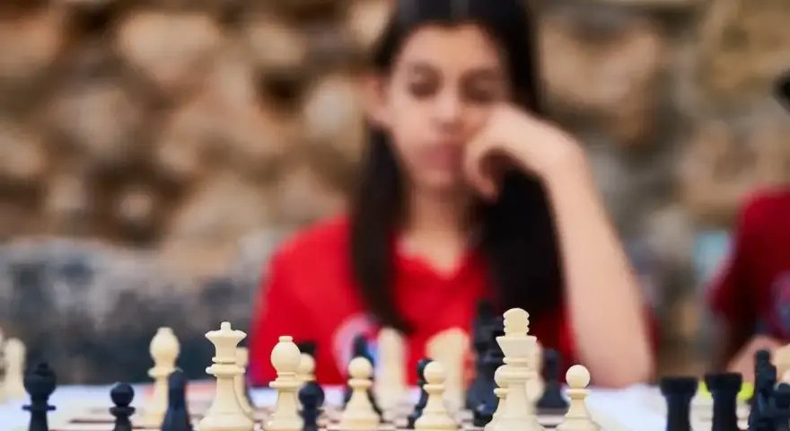 Niña pensativa frente a un tablero de ajedrez, inmersa en los juegos de decisiones.