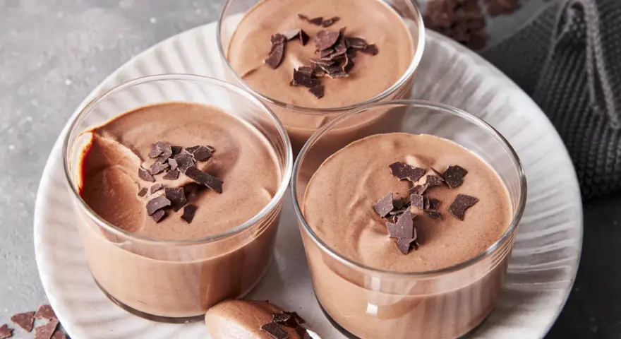 Drei Gläser mit luftiger Schokoladenmousse, garniert mit Schokostückchen. Ein Löffel zeigt die cremige Konsistenz dieses rezept mousse au chocolat ohne ei.