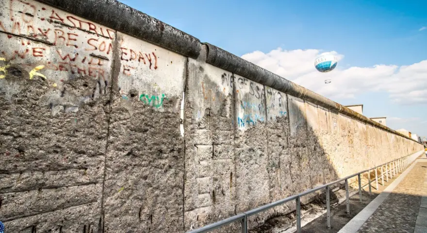 Beim Berlin Mauer besichtigen sieht man Graffiti und einen Heißluftballon.