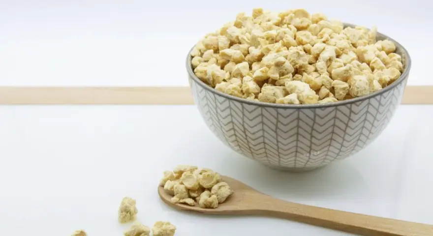 Un cuenco lleno de soja texturizada y una cuchara de madera con más de este ingrediente versátil.