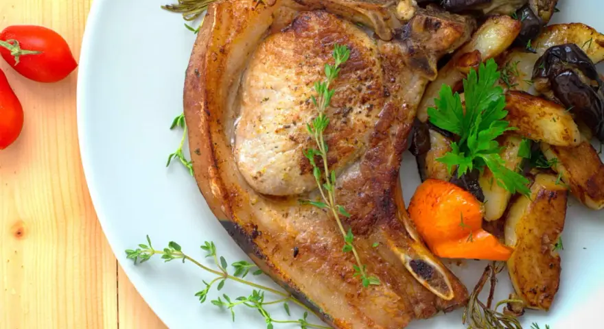 Une côte de porc savoureuse accompagnée de légumes rôtis, de pommes de terre et de tomates cerises.