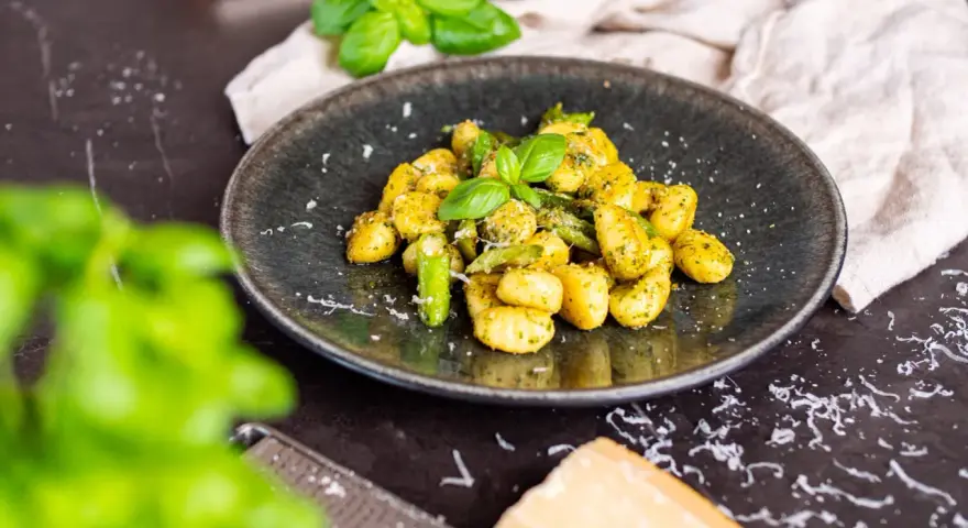 Gnocchi mit Spargel, garniert mit frischem Basilikum und Parmesan. Ein köstliches Gericht, das den Frühling auf den Teller bringt.