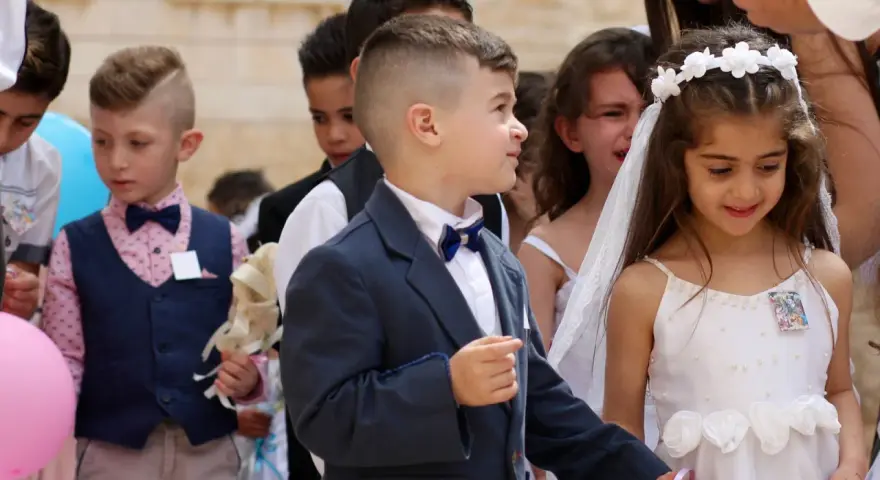 Chłopiec w eleganckim garniturze, z kokardką, wygląda jak z obrazka pin-up. Obok niego dziewczynka w białej sukience.