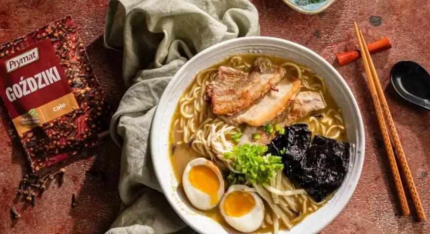 Jak zrobić ramen? Aromatyczny bulion, makaron, jajko na pół, plastry mięsa i nori. Obok paczka goździków Prymat.