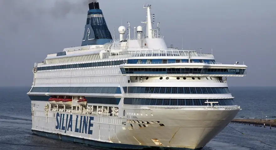 Ogromny prom pasażerski Silja Europa z charakterystycznym kominem i niebieskimi pasami na białym kadłubie płynie po spokojnym morzu.