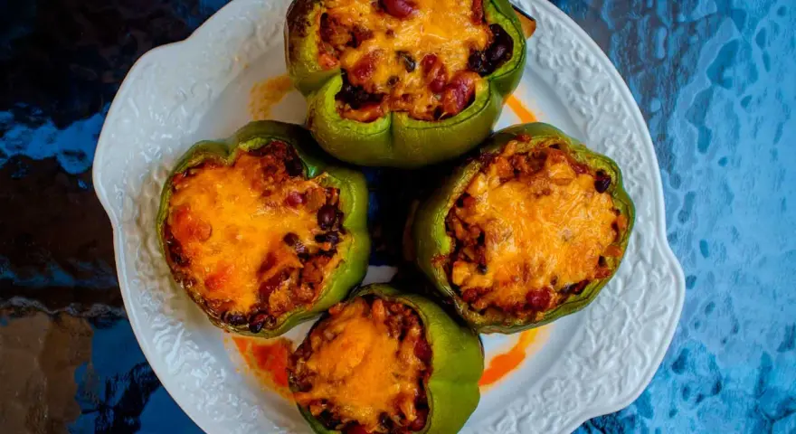 Cuatro pimientos verdes rellenos con carne, frijoles y arroz, cubiertos con queso derretido, servidos en un plato blanco.