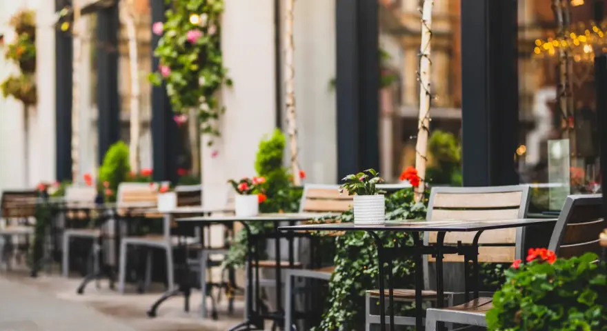 Mesas y sillas vacías en la terraza de un restaurante, adornadas con plantas y flores. Un lugar acogedor, listo para recibir clientes tras obtener las licencias de restaurantes.