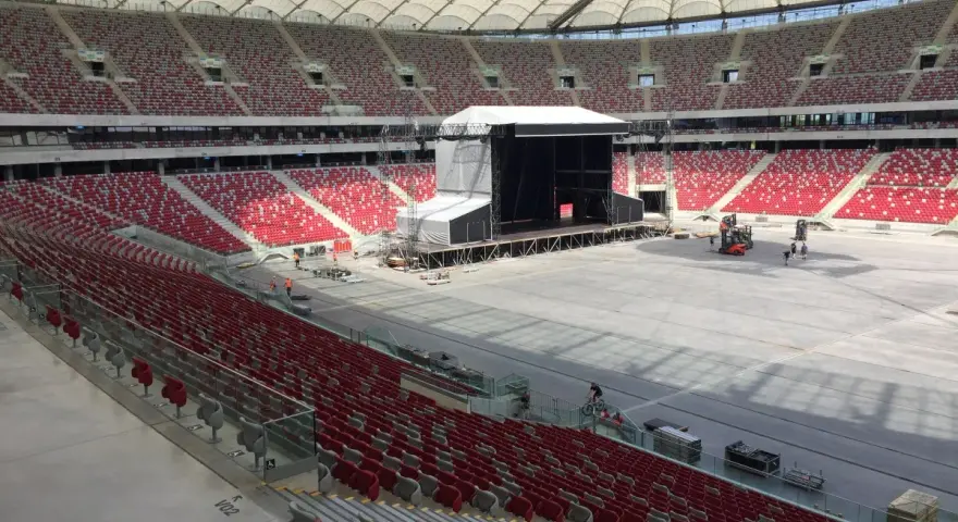 Przygotowania do koncertu Depeche Mode w Warszawie. Ogromny stadion z pustymi czerwonymi trybunami i sceną w budowie.