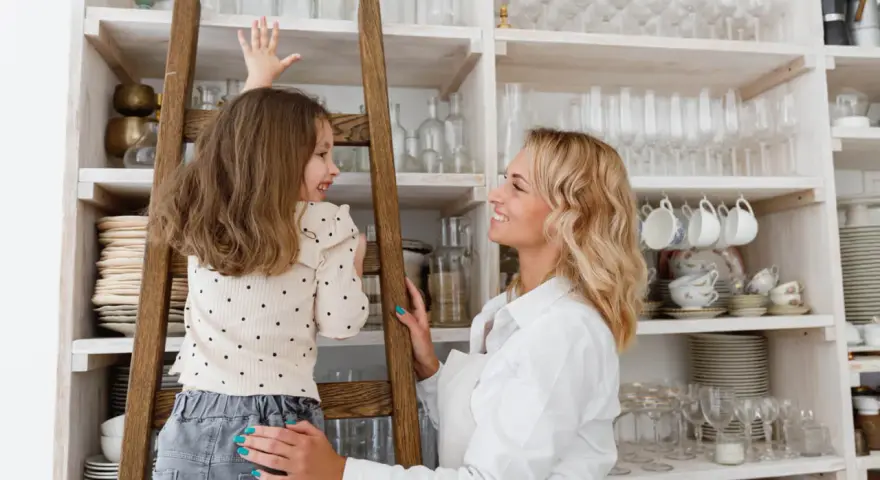 Mama i córka przy regale pełnym naczyń. W górnych szafkach kuchennych trzymamy rzadziej używane, ozdobne kieliszki i filiżanki.