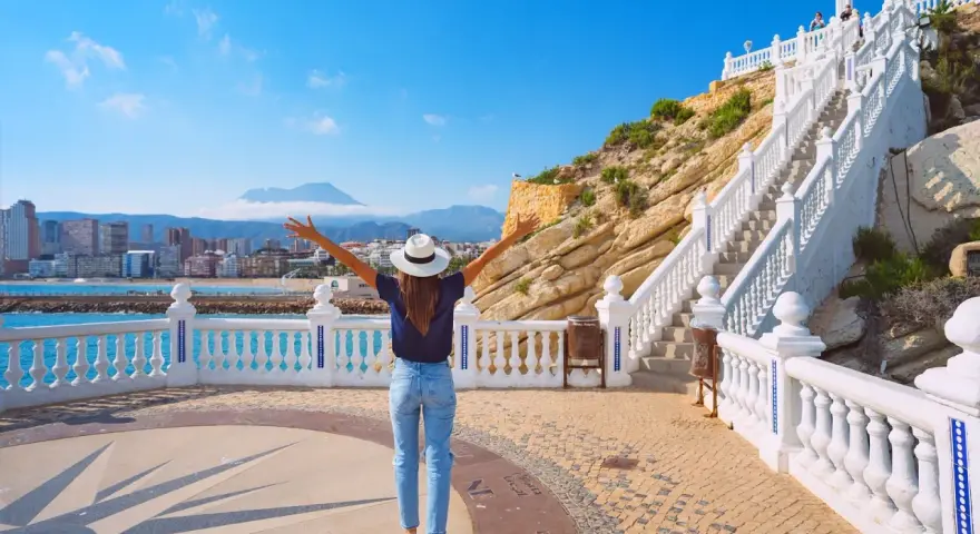 Mujer con brazos abiertos admira la vista de Benidorm desde el mirador. ¡Un lugar ideal que ver en Benidorm!