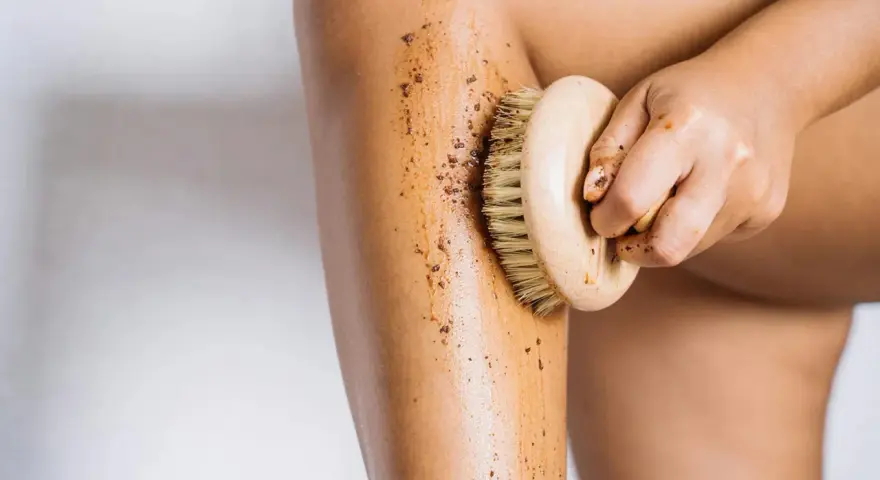 Exfoliación corporal con un cepillo de madera y un scrub para ayudar a como hidratar la piel desde dentro.