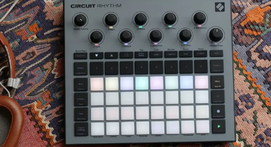 Szary kontroler Circuit Rhythm z podświetlanymi padami, gotowy do tworzenia muzyki. Słuchawki obok dopełniają scenę.