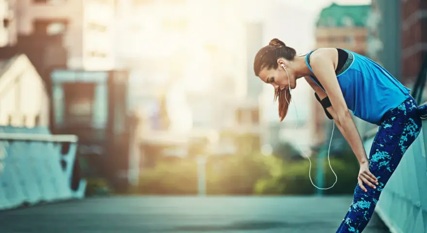 Atleta esausta appoggiata a un corrimano, con le cuffie. Potrebbe aver bisogno di rimedi per il sovrallenamento.