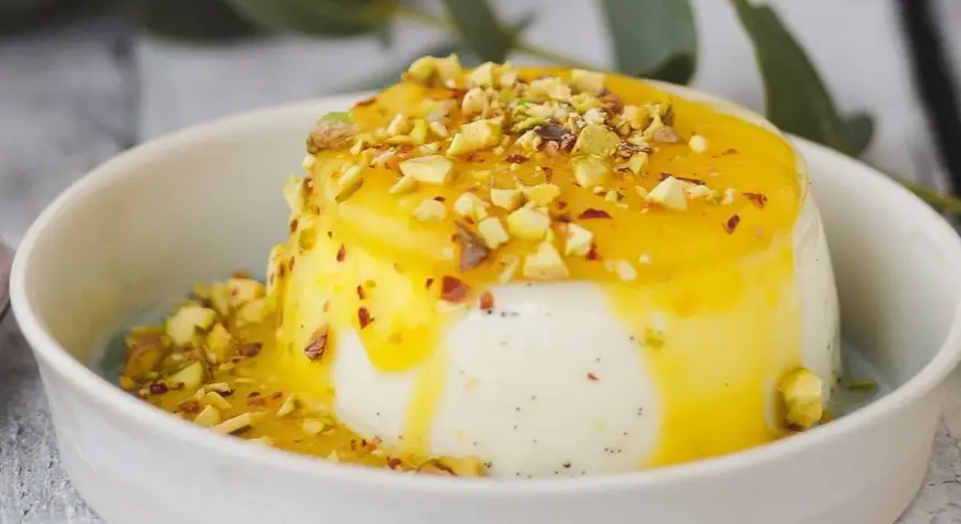 Budino fatto in casa cremoso, con salsa gialla e granella di pistacchi, servito in una ciotola bianca.