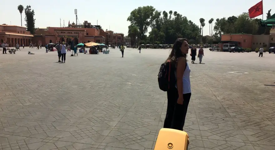 Una mujer con mochila y maleta amarilla en una plaza de Marruecos. Piensa en qué llevar a Marruecos para este viaje.