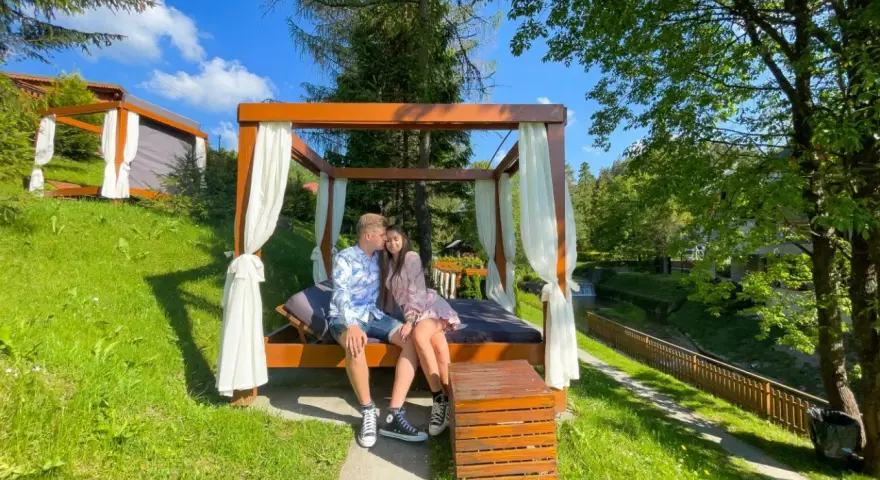 Idealne miejsce, gdzie na weekend we dwoje. Para odpoczywa na łóżku pod baldachimem w otoczeniu zieleni.