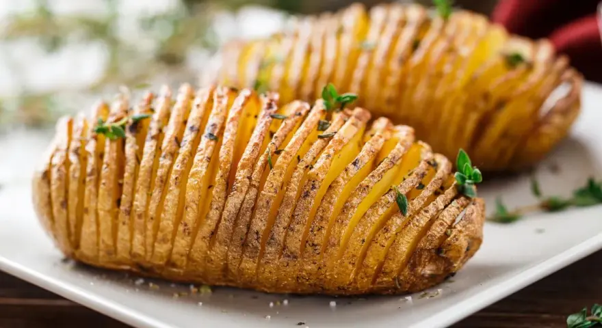 Patate hasselback dorate e croccanti, appena sfornate dalla friggitrice ad aria, guarnite con erbe aromatiche fresche.
