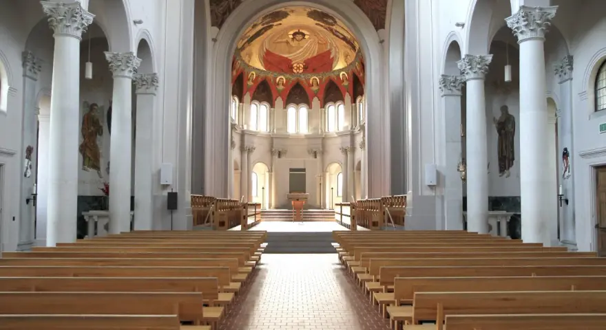 Interior of a grand abbey, with rows of wooden pews leading to an altar. The domed ceiling features a vibrant fresco. Check the abbey mass schedule for service times.
