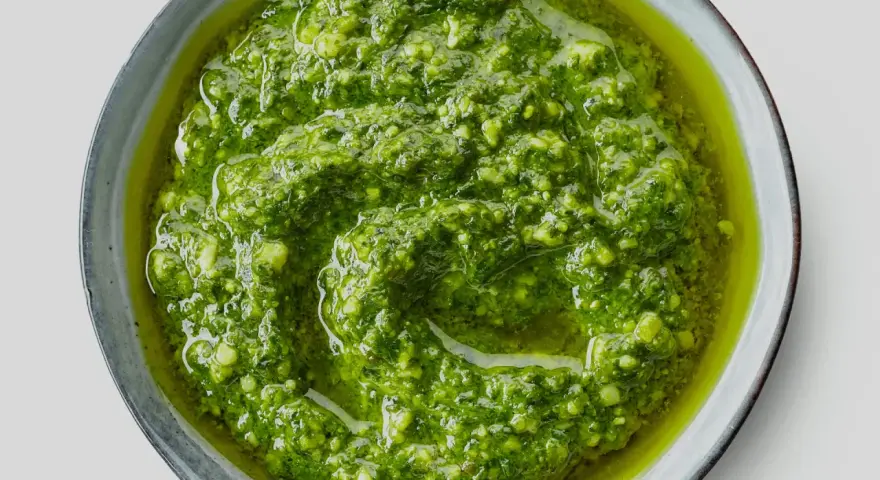 Närbild på hemmagjord pesto i en skål. Oljan flyter runt den gröna, grovhackade peston. Perfekt för att förlänga hållbarheten.