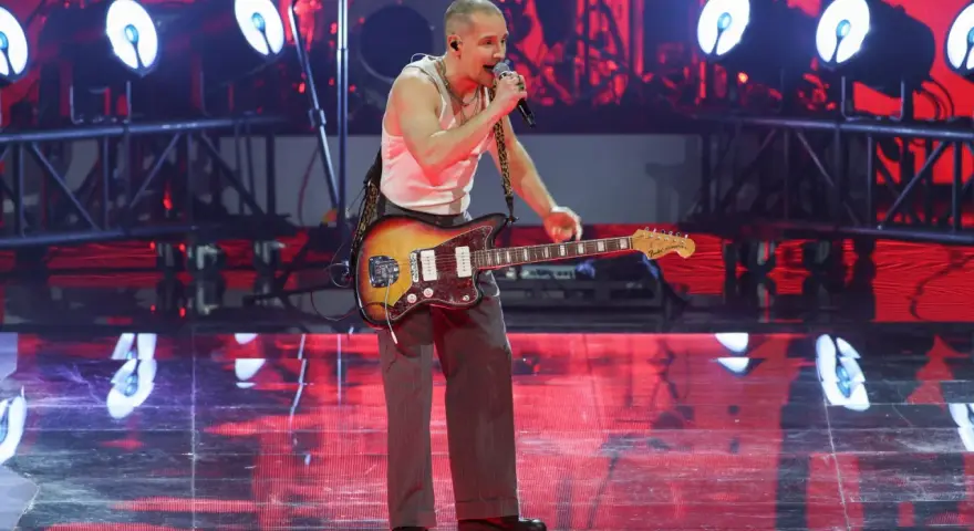 Krzysztof Zalewski na koncercie, śpiewa i gra na gitarze. Scena oświetlona czerwonymi światłami.