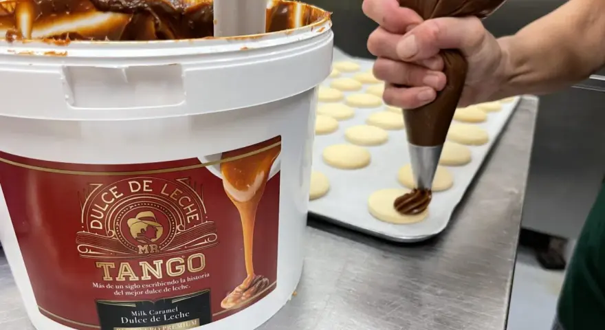 Un repostero decora galletas con una manga pastelera, usando el delicioso dulce de leche de un gran envase.