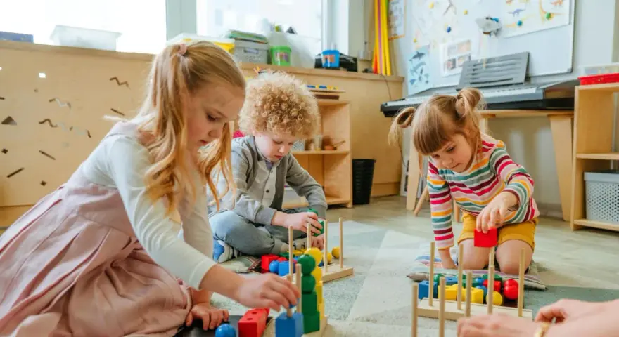 Drei Kinder, darunter ein **kind 8 jahre**, spielen konzentriert mit bunten Holzbausteinen im Kindergarten.