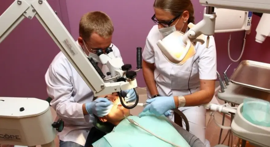 Dentysta i asystentka pracują przy pacjencie z użyciem mikroskopu stomatologicznego.