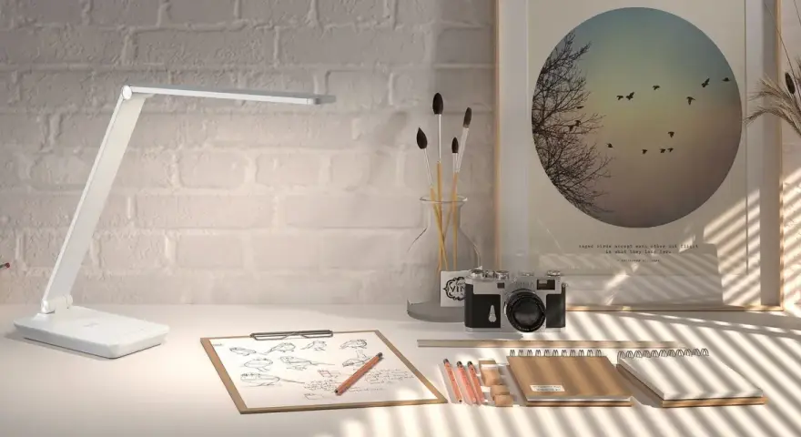 Lámpara LED moderna sobre un escritorio con bocetos de pájaros, cámara antigua y un póster inspirador. La luz es ideal para estudiar.