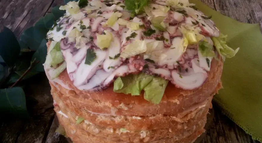 Panettone Gastronomico with sliced octopus, lettuce, and herbs on a wooden table.