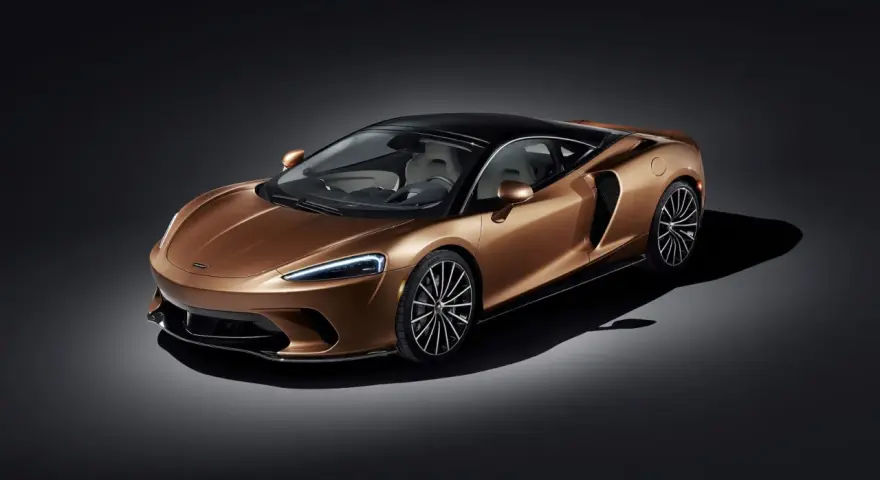 Elegancki, miedziany McLaren GT z czarnym dachem i felgami, prezentujący swoje sportowe linie na ciemnym tle.