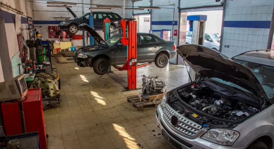 Warsztat samochodowy z kilkoma autami na podnośnikach, w tym ciemnym sedanem, który wygląda jak p1351 peugeot. Silnik wyjęty z jednego z pojazdów.