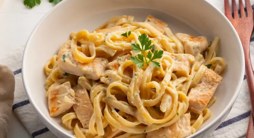 Pyszny kurczak w sosie alfredo z tagliatelle, udekorowany natką pietruszki. Idealny obiad dla całej rodziny.