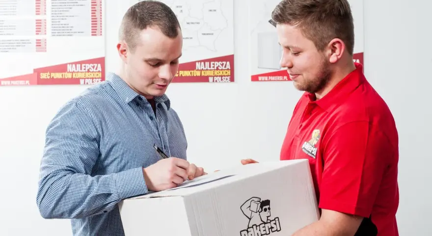 Kurier w czerwonej koszulce przekazuje paczkę, a klient podpisuje dokument. Zastanawiasz się, ile zarabia kurier?