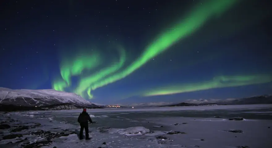 En ensam person står på en isig strand och ser på det magiska abisko norrsken som dansar över himlen.