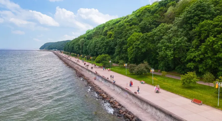 Spacer po molo południowym wzdłuż zielonego wybrzeża. Ludzie spacerują, odpoczywają na ławkach, ciesząc się pięknym dniem nad morzem.