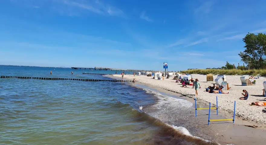 En solig tysk strand med folk som njuter av havet och sanden. En brygga sträcker sig ut i vattnet.